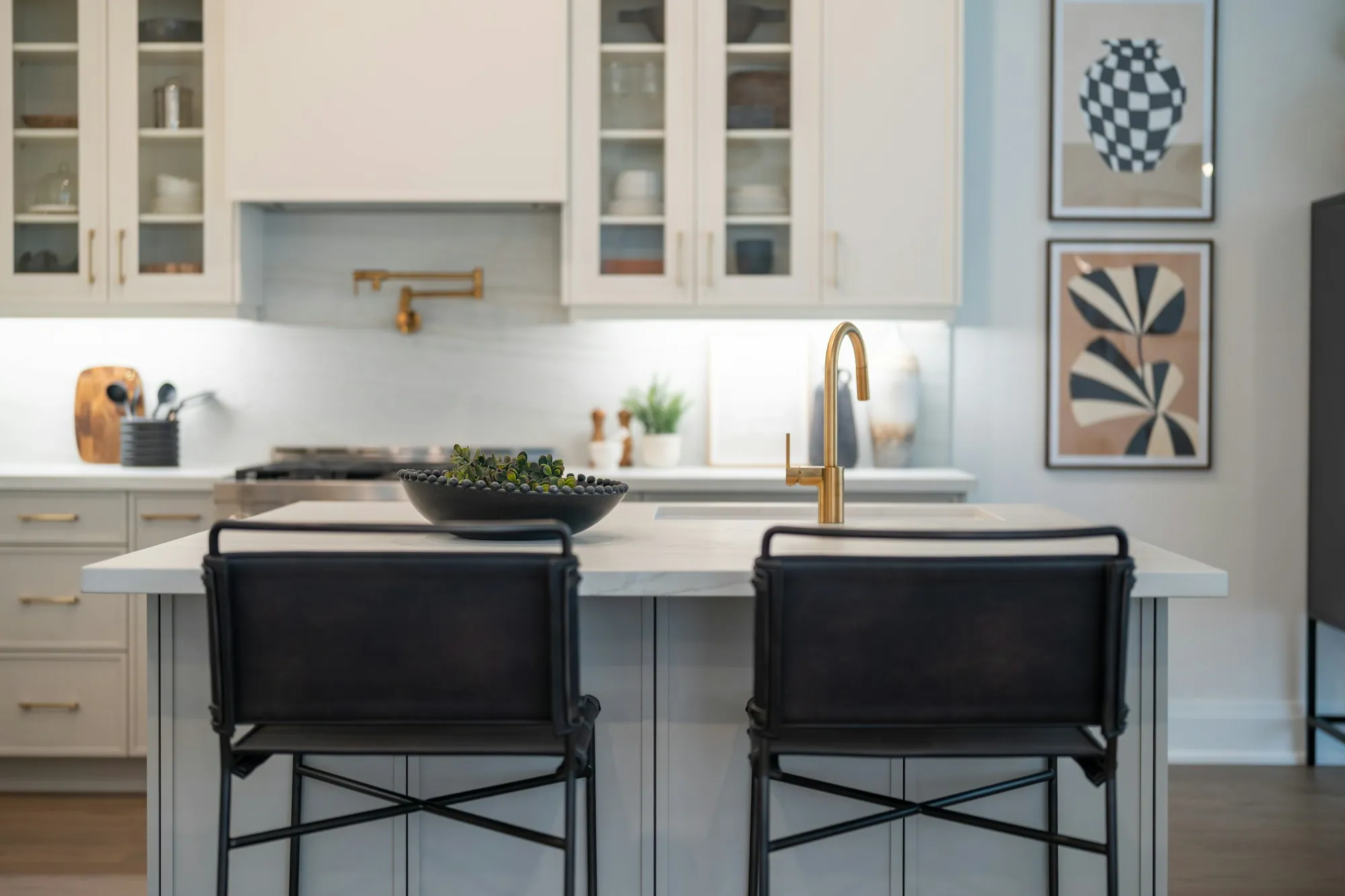 Kitchen island with white counters, glass-front cabinets and black bar stools