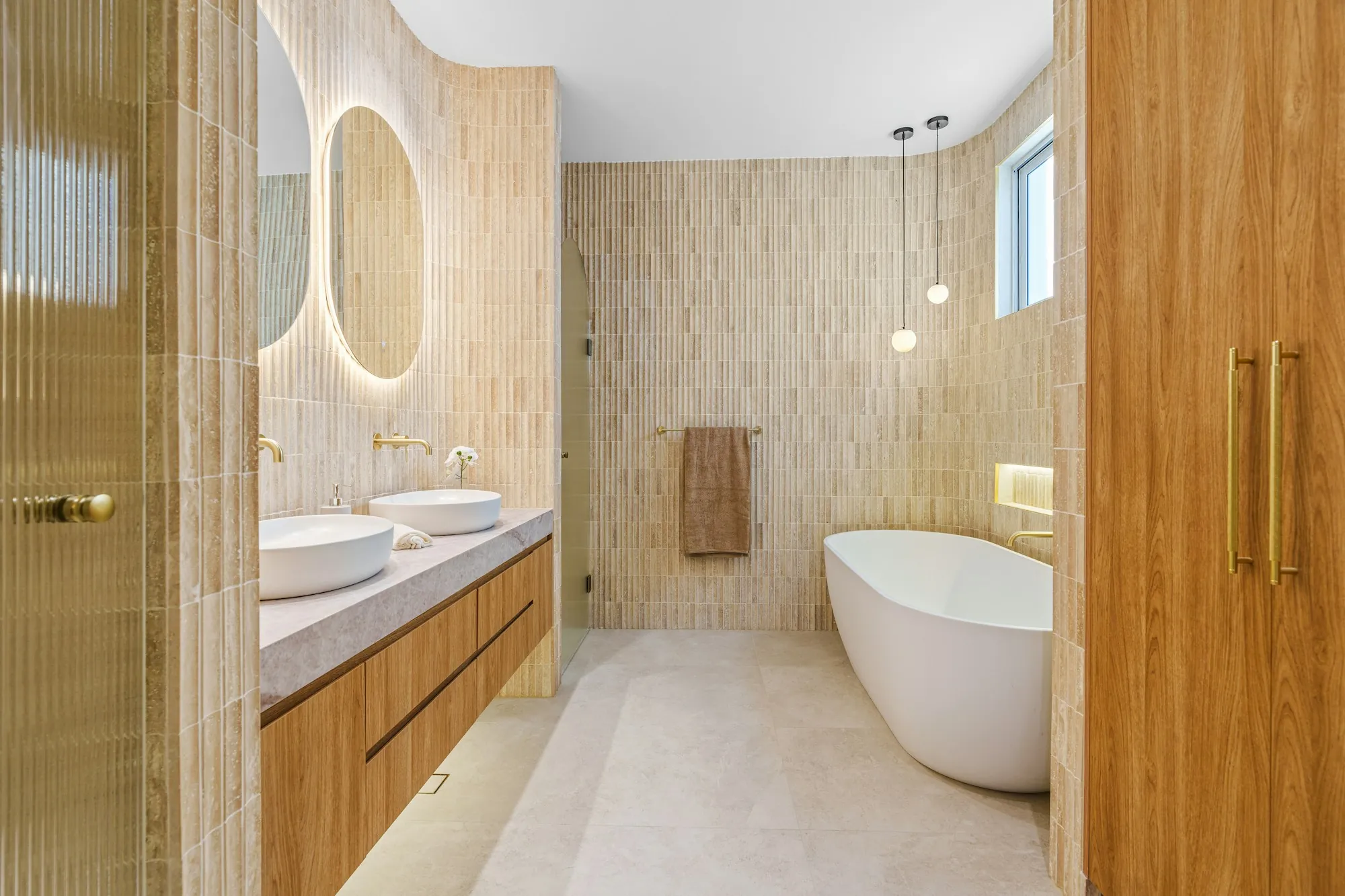 Remodeled bathroom with a freestanding tub, double vessel sinks and textured tile walls